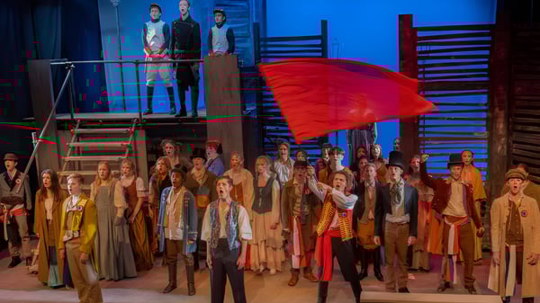 Schüler des Eastbourne College in traditionellen bunten Kostümen stehen auf einer Bühne mit rotem Schild.