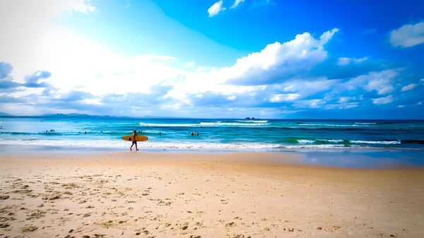 Ein Surfer läuft am sonnigen Strand entlang unter blauem Himmel auf dem Gelände der Eastern Fleurieu R-12 School.