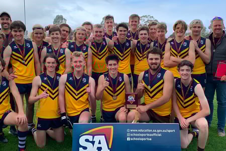 Eine Gruppe von Schülern der Eastern Fleurieu R-12 posiert als Sportsteam auf einem Feld mit Bergen im Hintergrund.