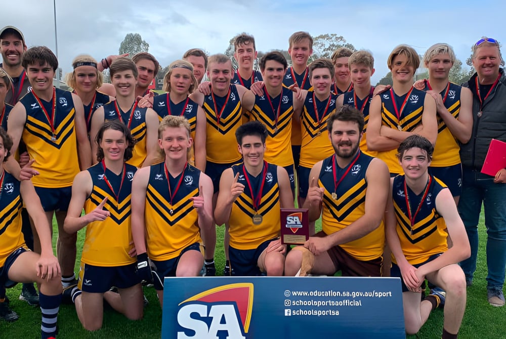 Eine Gruppe von Schülern der Eastern Fleurieu R-12 posiert als Sportsteam auf einem Feld mit Bergen im Hintergrund.