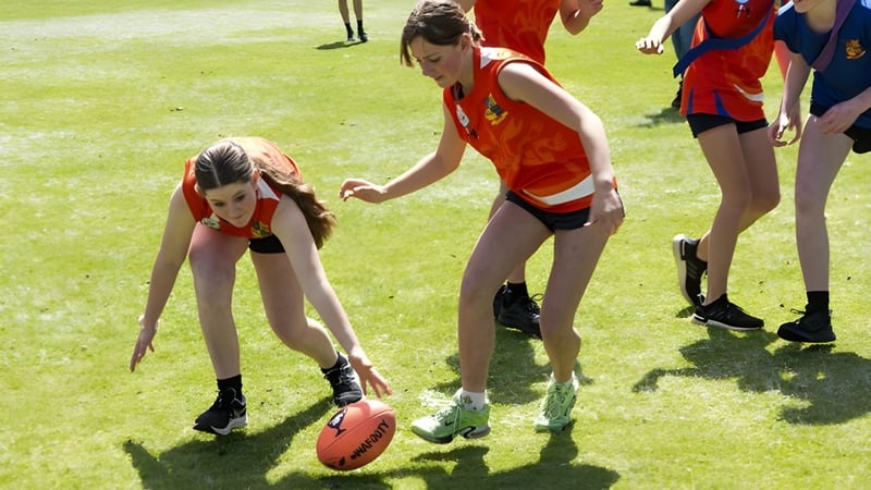 Zwei Schülerinnen der Eastern Hills Senior High School spielen auf einem Sportfeld, im Hintergrund sind weitere Personen zu sehen.