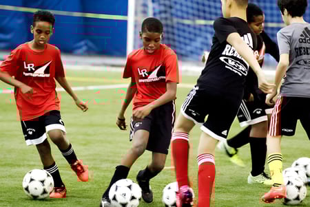 Eine Gruppe junger Fußballspieler in roten und schwarzen Trikots spielt auf dem Sportplatz der Eastern Ontario Public Schools.