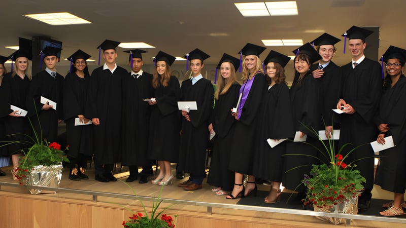 Eine Gruppe von Absolventinnen und Absolventen der Eastside Secondary School steht in einem Raum mit Pflanzen und Beleuchtung.