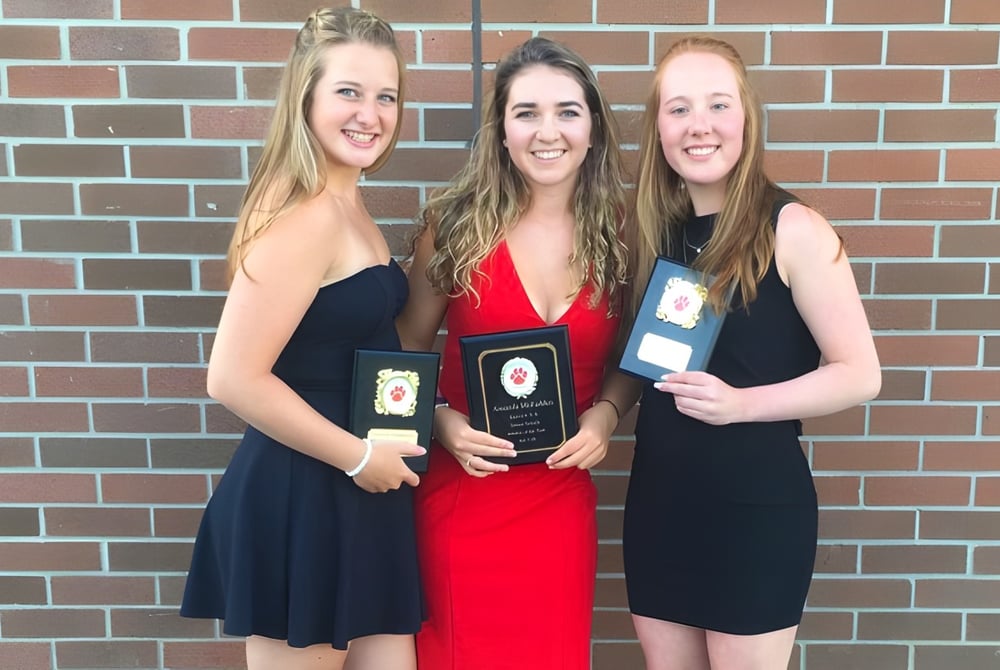 Drei Schülerinnen der Eastview Secondary School stehen vor einer Backsteinwand und halten Auszeichnungen in den Händen.