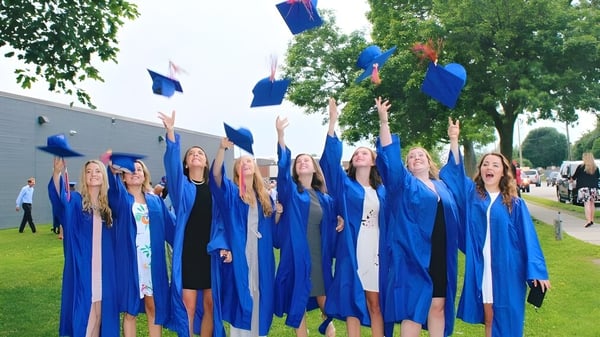 Eine Gruppe von Absolventinnen und Absolventen wirft ihre blauen Abschlussmützen auf dem Campus der Eastview Secondary School in die Luft.