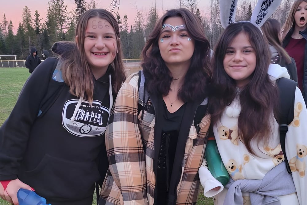 Vier Schülerinnen stehen auf einer Wiese vor einem Waldgebiet auf dem Gelände der École Arc-en-ciel.