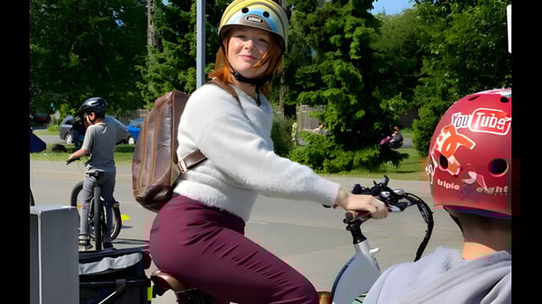 Eine Schülerin der École Au-coeur-de-l'île fährt mit Helm auf einem Fahrradweg umgeben von Bäumen und weiteren Radfahrern.