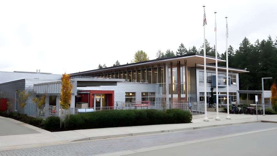 Das moderne Gebäude der École Au-coeur-de-l'île mit amerikanischer Flagge im Vordergrund und Bäumen im Hintergrund.