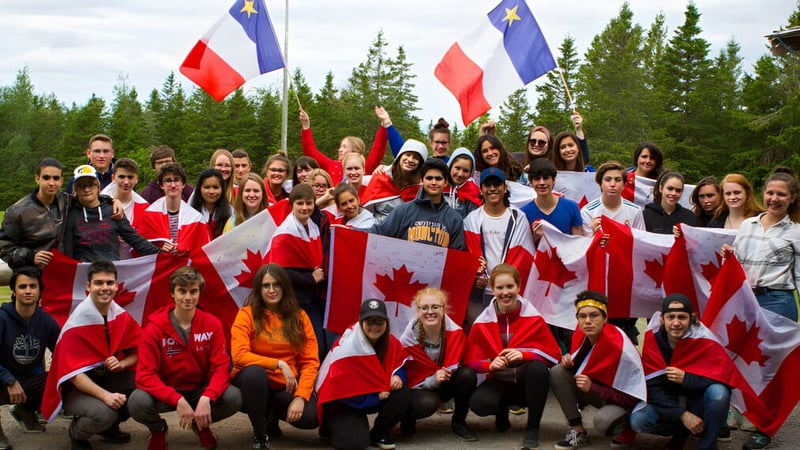 Eine Gruppe von Schülerinnen und Schülern der École Aux quatre vents hält kanadische und EU-Flaggen in einer bewaldeten Landschaft.