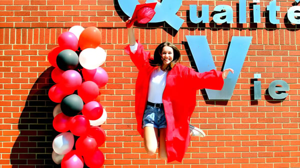 Eine Frau in rotem Outfit steht vor einer bunten Ballonwand an der École Aux quatre vents.