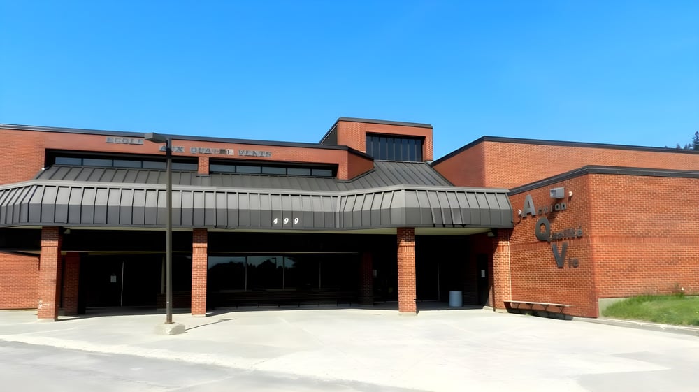 Das moderne Backsteingebäude mit großen Glasfenstern auf dem Campus der École Aux quatre vents unter klarem Himmel.