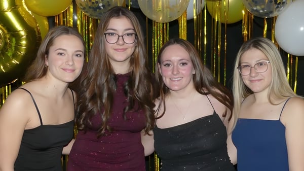 Vier Schülerinnen in formeller Kleidung posieren vor goldenen und silbernen Ballons auf dem Campus der École Clément-Cormier.