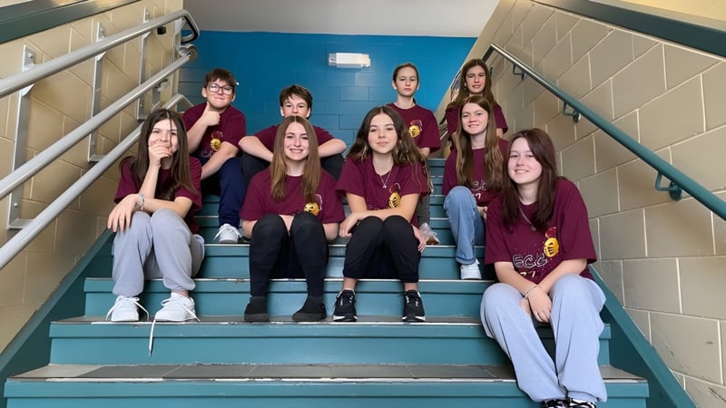 Eine Gruppe von Schülerinnen der École Clément-Cormier sitzt auf der Treppe im Schulflur vor blauen und grauen Wänden.