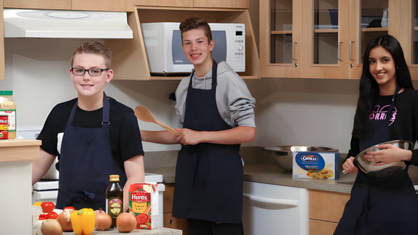 Drei Schüler der École Dansereau Meadows School stehen in der Schulküche und bereiten Lebensmittel zu.