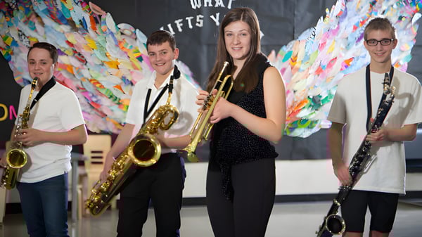 Eine Gruppe Musiker steht vor einem bunten abstrakten Hintergrund auf dem Campus der École Dansereau Meadows School.