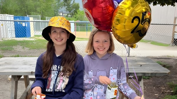 Zwei Schülerinnen der École de l'Anse-au-sable stehen im Freien und halten bunte Luftballons in der Hand.