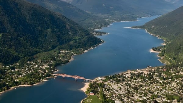 Eine Luftaufnahme zeigt einen See mit einer Brücke und bewaldeten Bergen in der Umgebung der École des Sentiers-Alpins.