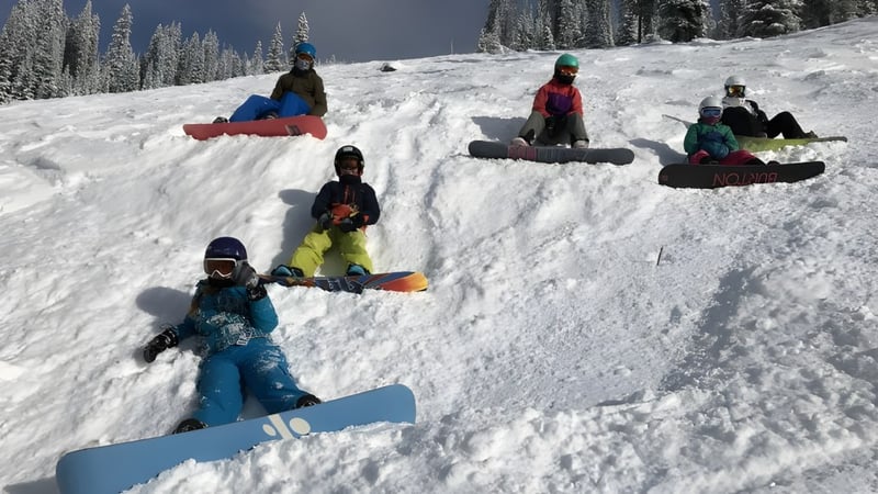 Schüler der École des Sentiers-Alpins fahren auf Snowboards einen schneebedeckten Abhang im Winterwald hinunter.