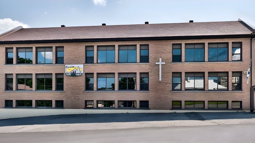Das mehrstöckige Backsteingebäude der École des Sept Sommets steht in einem urbanen Bereich mit gepflastertem Vorplatz.