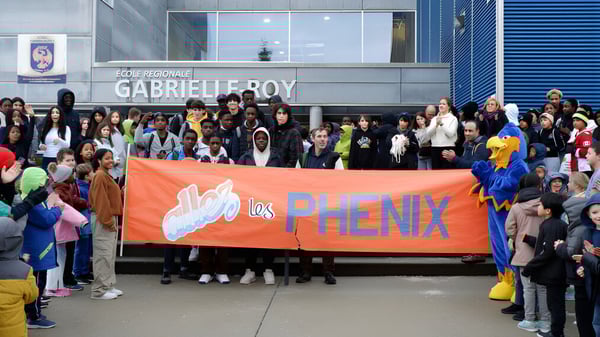 Schüler der École Gabrielle-Roy halten ein großes orangefarbenes Banner mit der Aufschrift Los Phenix vor dem Schulgebäude.