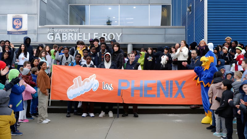 Schüler der École Gabrielle-Roy halten ein großes orangefarbenes Banner mit der Aufschrift Los Phenix vor dem Schulgebäude.