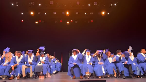 Eine Gruppe von Absolventen der École secondaire publique Gisèle-Lalonde steht in blauen Talaren auf einer Bühne mit beleuchtetem Hintergrund.