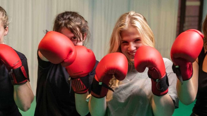 Vier Schülerinnen der École Jeannine Manuel mit roten Boxhandschuhen in einem schwach beleuchteten Raum.