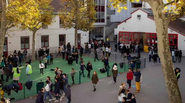 Menschen spazieren auf einem mit grünem Teppich bedeckten Weg zwischen buntem Herbstlaub nahe der École Jeannine Manuel.