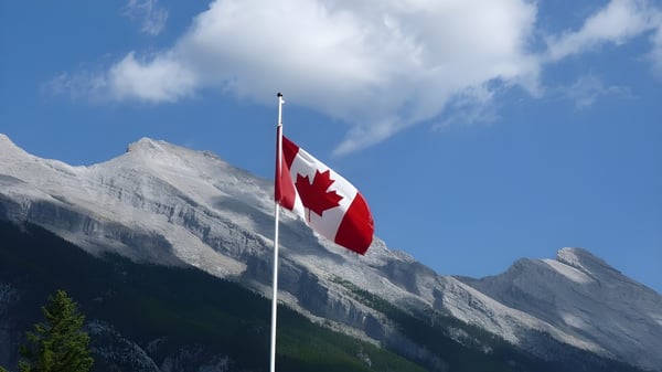 Eine kanadische Flagge weht vor schneebedeckten Bergen auf dem Gelände der École L’Odyssée.