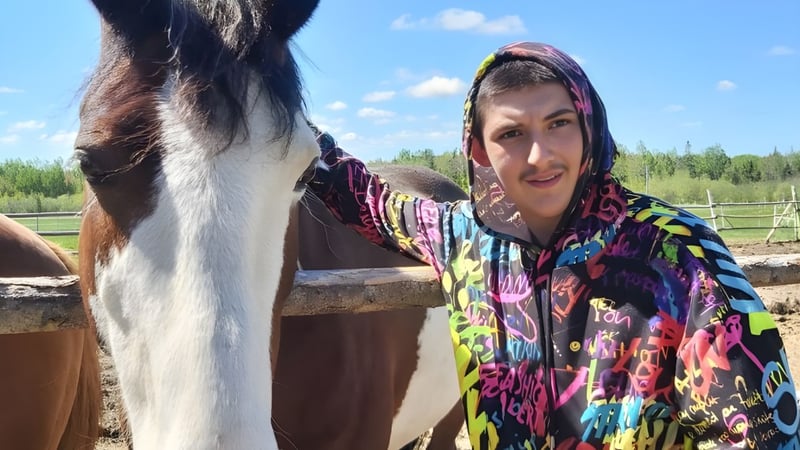 Eine Frau steht neben einem großen braunen Pferd auf dem Außengelände der École Marie-Esther vor bewaldetem Hintergrund.