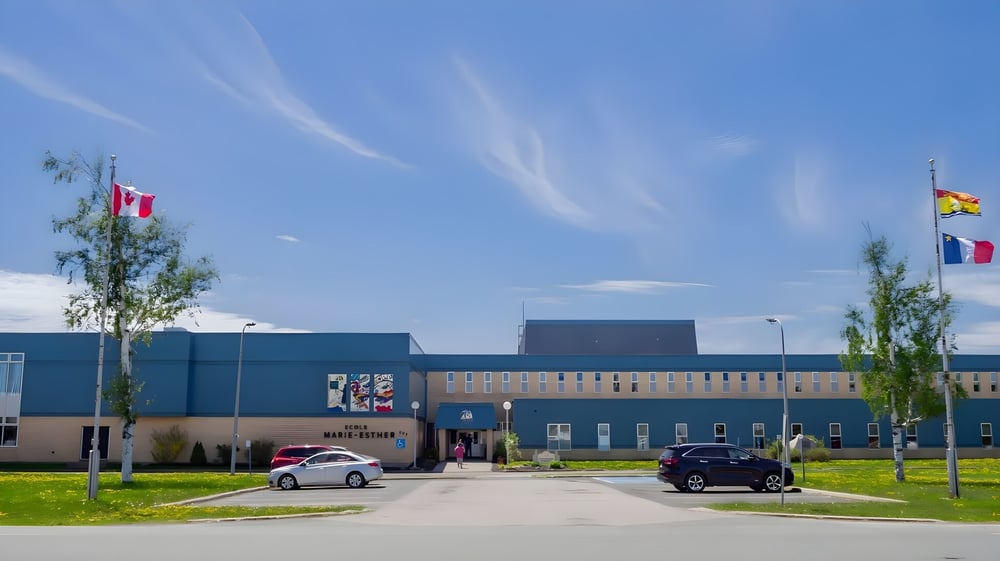 Das moderne mehrstöckige Gebäude der École Marie-Esther ist von einer Wiese mit Bäumen und geparkten Autos umgeben.