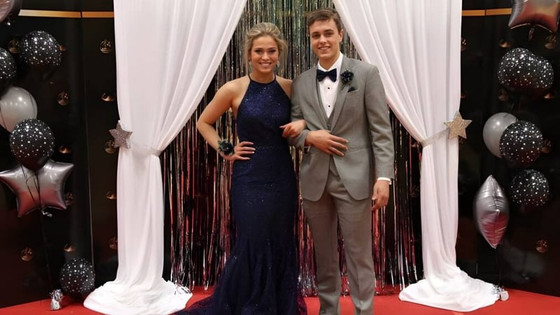 Ein junges Paar steht vor einem dekorativen Hintergrund mit Vorhaengen und Luftballons auf dem Campus der École Marie-Esther.