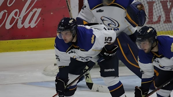 Zwei Hockeyspieler in Uniform spielen auf dem Eis vor einer Coca-Cola-Werbung auf dem Gelände der École Mathieu-Martin.