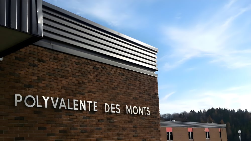 Das moderne Backsteingebäude der École Polyvalente des Monts steht vor blauem Himmel und bewaldeten Hügeln.