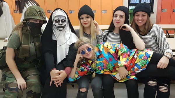 Eine Gruppe Schülerinnen der École Polyvalente des Monts trägt verschiedene Kostüme und posiert gemeinsam in einer schulischen Umgebung.