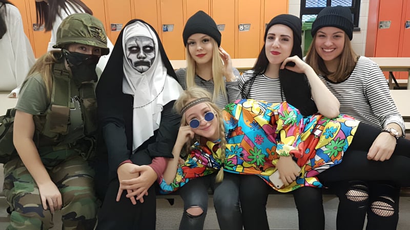 Eine Gruppe Schülerinnen der École Polyvalente des Monts trägt verschiedene Kostüme und posiert gemeinsam in einer schulischen Umgebung.