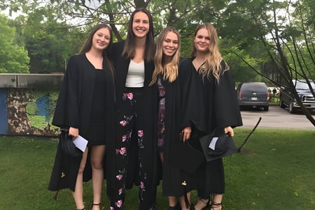 Vier Schülerinnen stehen gemeinsam im Freien auf dem Rasen der École Polyvalente Secondaire Curé-Mercure vor einer Graffiti-Wand.