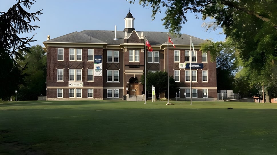 Das mehrstöckige Backsteingebäude mit Uhrturm auf dem Gelände der École secondaire publique Rivière Rideau ist von Bäumen und einer Wiese umgeben.