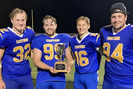 Vier Schüler der École Sainte-Anne tragen Fußballtrikots und halten einen Pokal auf dem Fußballfeld bei Nacht.
