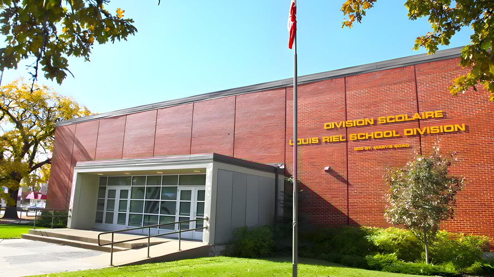 Das Backsteingebäude der École secondaire publique Louis-Riel ist von Bäumen und einer Rasenfläche umgeben.