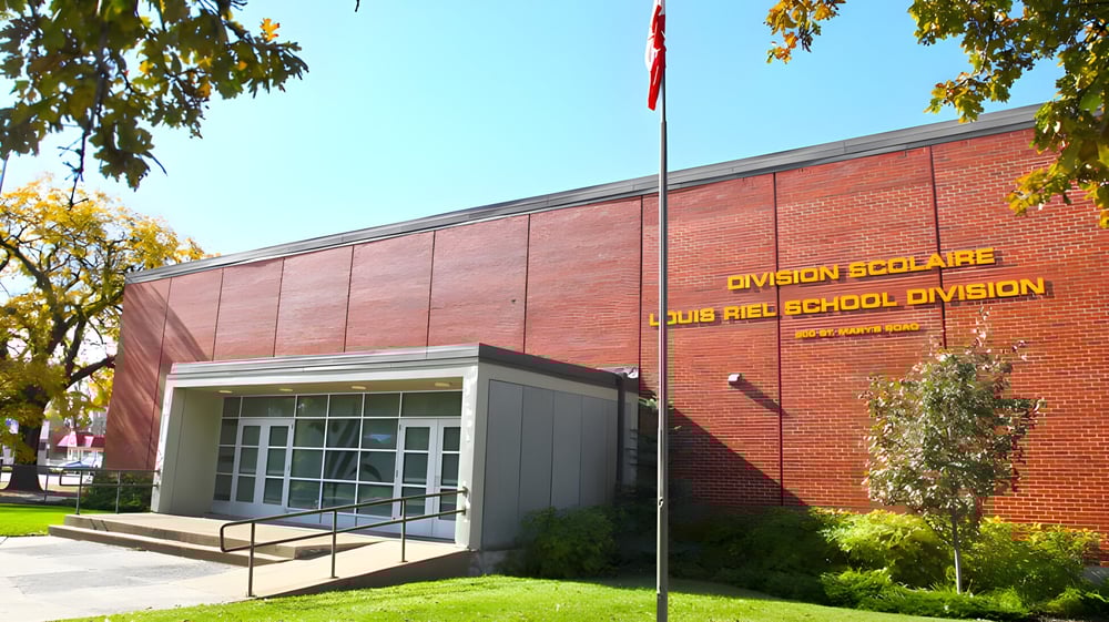 Das Backsteingebäude der École secondaire publique Louis-Riel ist von Bäumen und einer Rasenfläche umgeben.