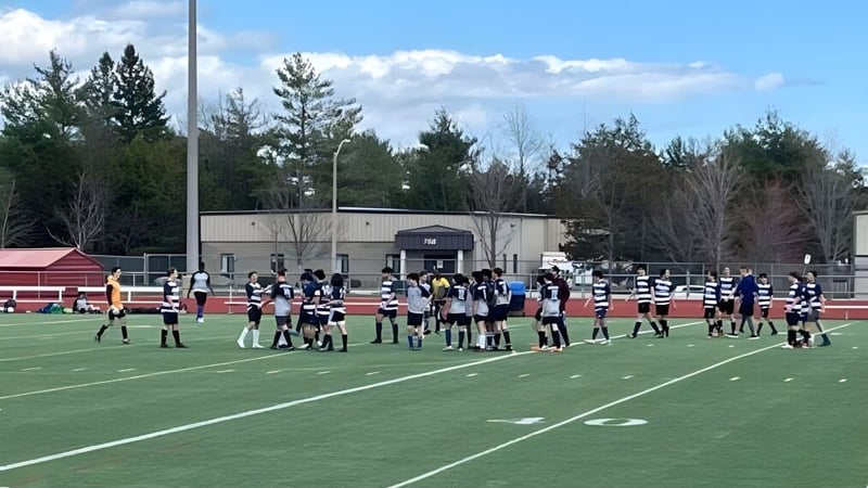 Eine Sportmannschaft der École secondaire publique Mille-îles versammelt sich auf einem Rasenfeld mit Kiefern und einem Gebäude im Hintergrund.