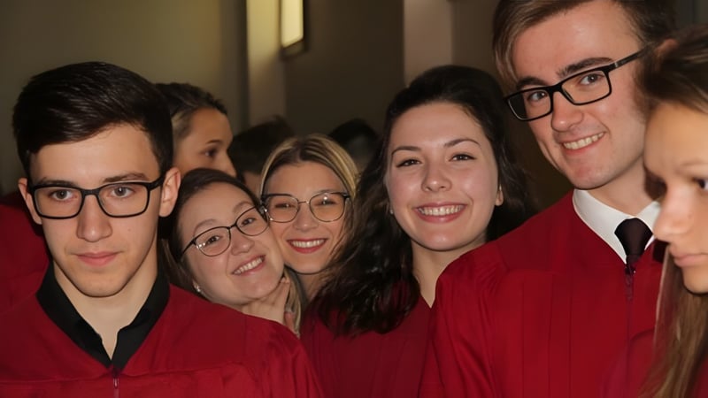Eine Gruppe von Absolventinnen und Absolventen in roten Talaren posiert gemeinsam auf dem Campus der École secondaire Népisiguit.