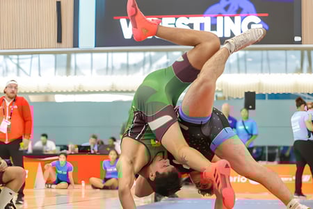 Eine weibliche Ringerin in roter und grüner Uniform führt einen akrobatischen Move auf der Matte bei einem Wettkampf der École secondaire Népisiguit aus.