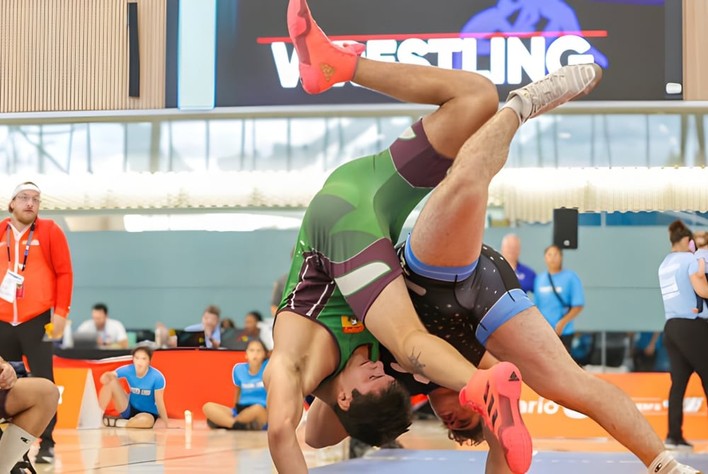 Eine weibliche Ringerin in roter und grüner Uniform führt einen akrobatischen Move auf der Matte bei einem Wettkampf der École secondaire Népisiguit aus.