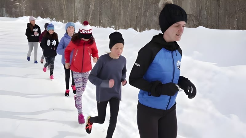 Schüler der École Sophie Morigeau gehen in warmer Winterkleidung durch einen verschneiten Wald mit kahlen Bäumen.