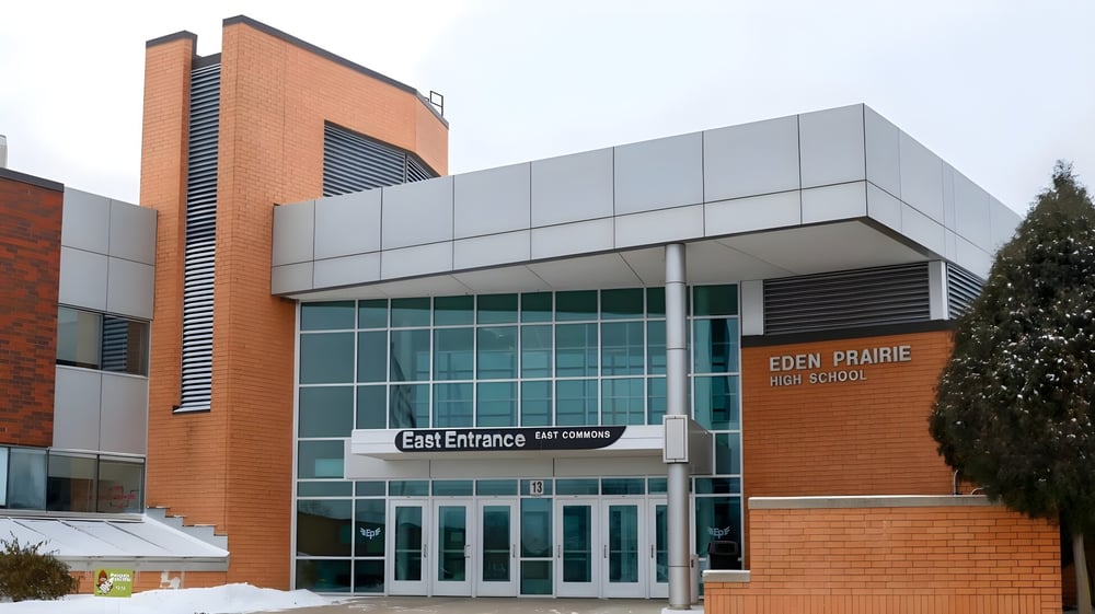 Das moderne mehrstöckige Schulgebäude der Eden Prairie Schools mit Glasfenstern und markantem Eingang ist von Bäumen umgeben.