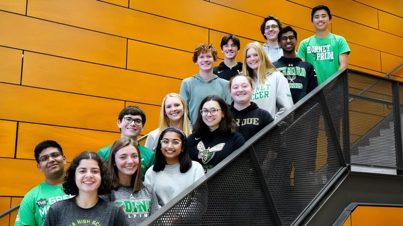 Eine Gruppe Schüler steht auf einer Treppe vor einer orangefarbenen Wand auf dem Campus der Edina Public Schools.