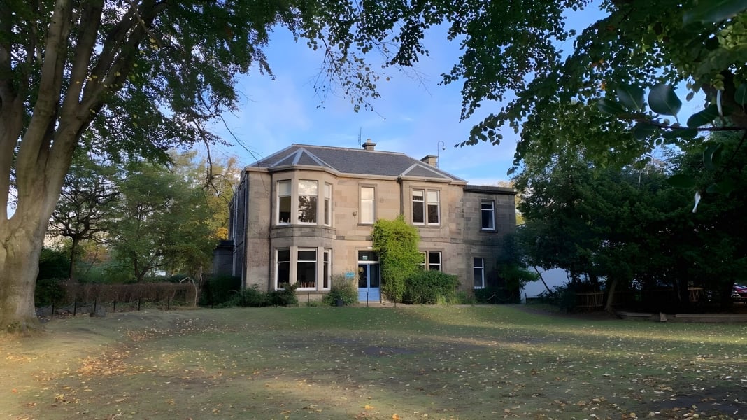 Das Backsteingebäude der Edinburgh Steiner School steht umgeben von herbstlichen Bäumen und Laub auf dem Schulgelände.
