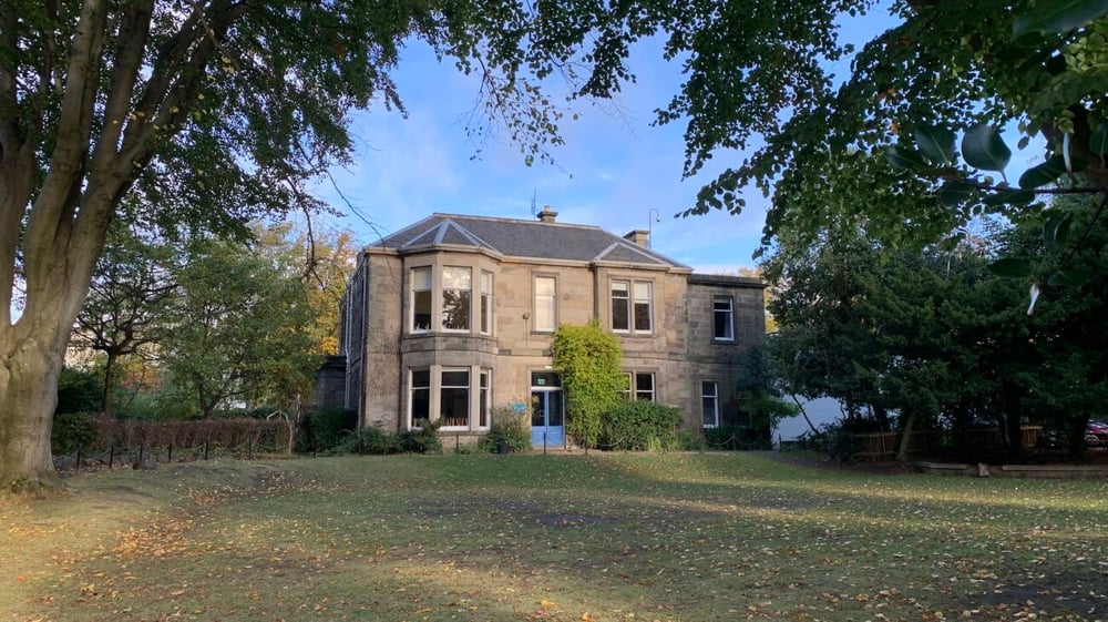 Das Hauptgebäude der Edinburgh Steiner School steht umgeben von herbstlich gefärbten Bäumen auf einem großen Grundstück.